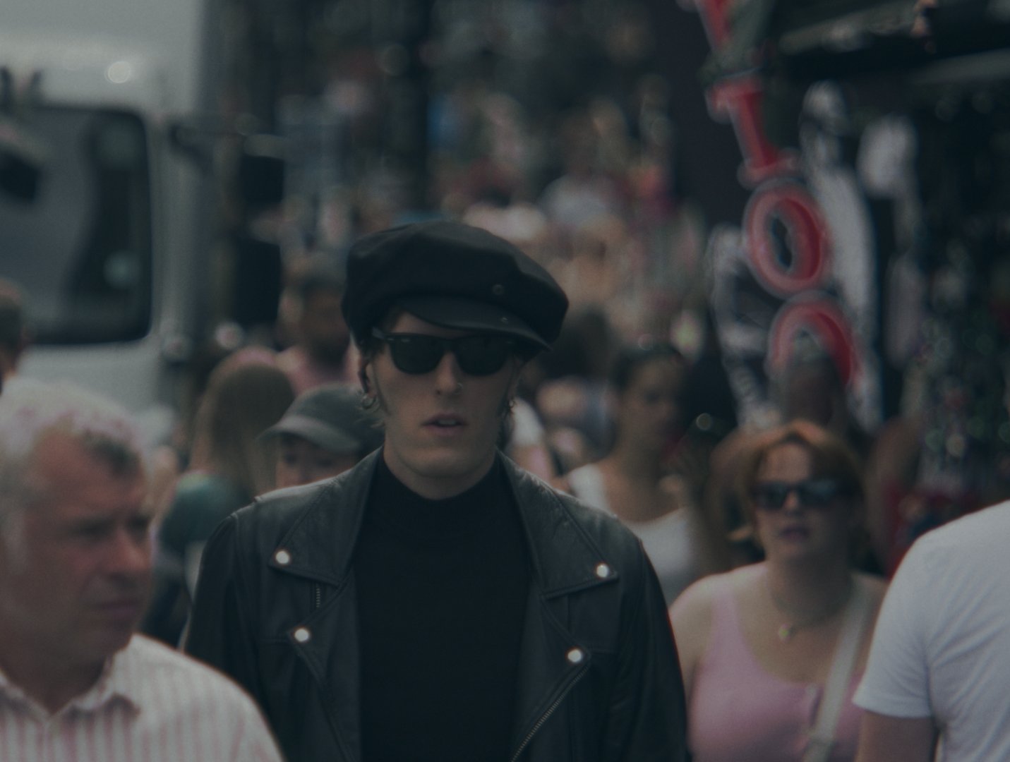 Matty James Cassidy walking towards camera through a crowded Camden street, the crowd blurred around him.