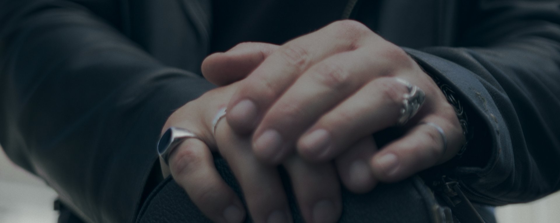 Close on a pair of ringed hands folded over a bag.