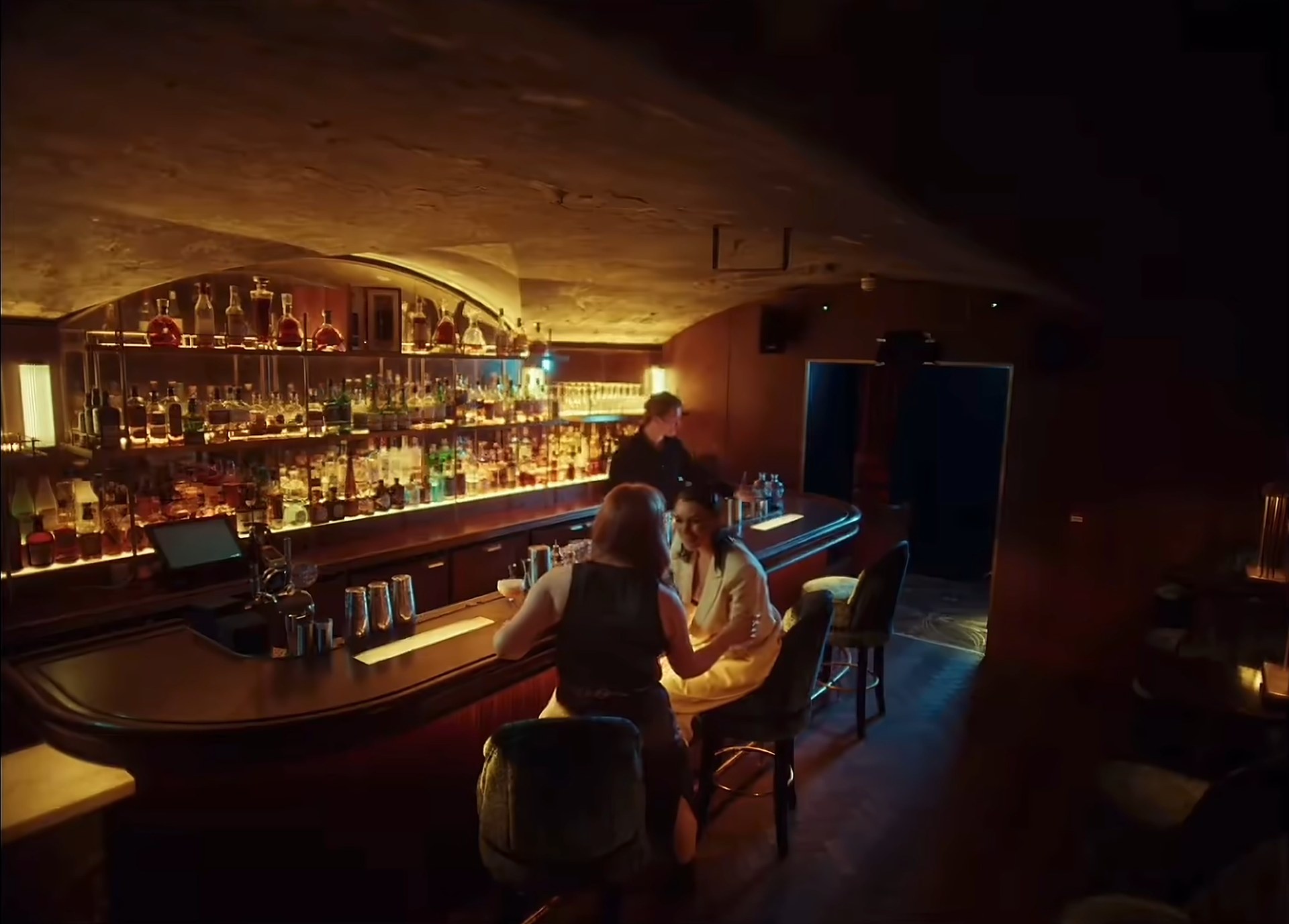 A low-lit bar, bottles ranked behind the counter, a couple at the far end.