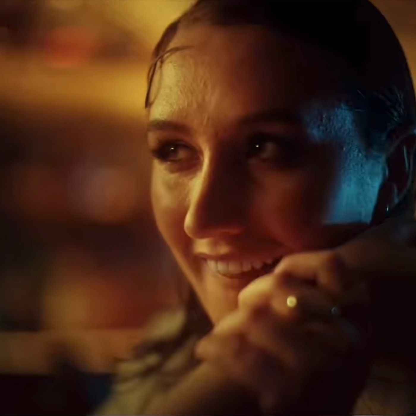 A woman smiling, chin resting on her hand, warm light across her face.