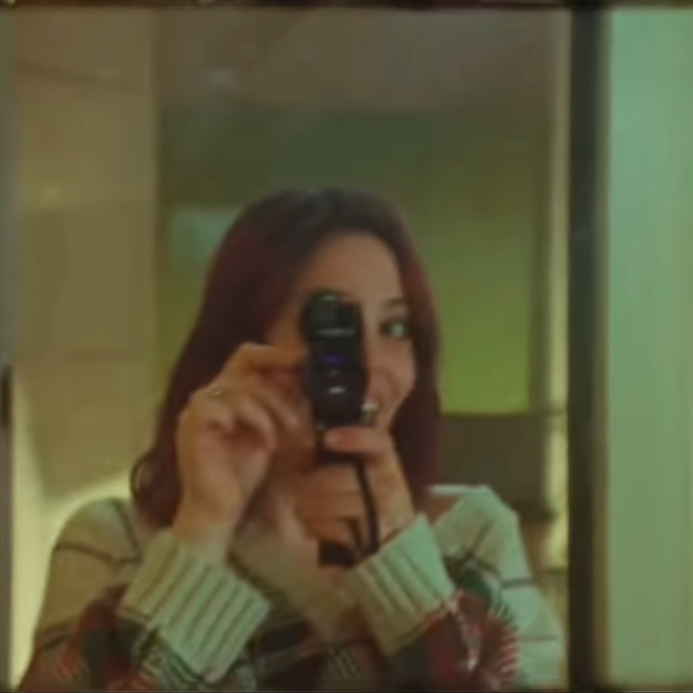 A woman filming on a small camcorder, caught in a doorway.
