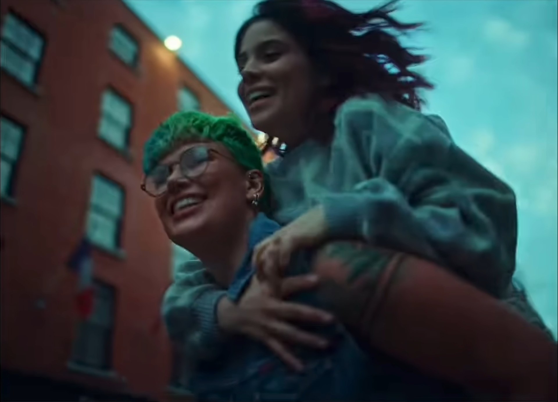 Two people laughing, one carrying the other, a brick street at dusk.