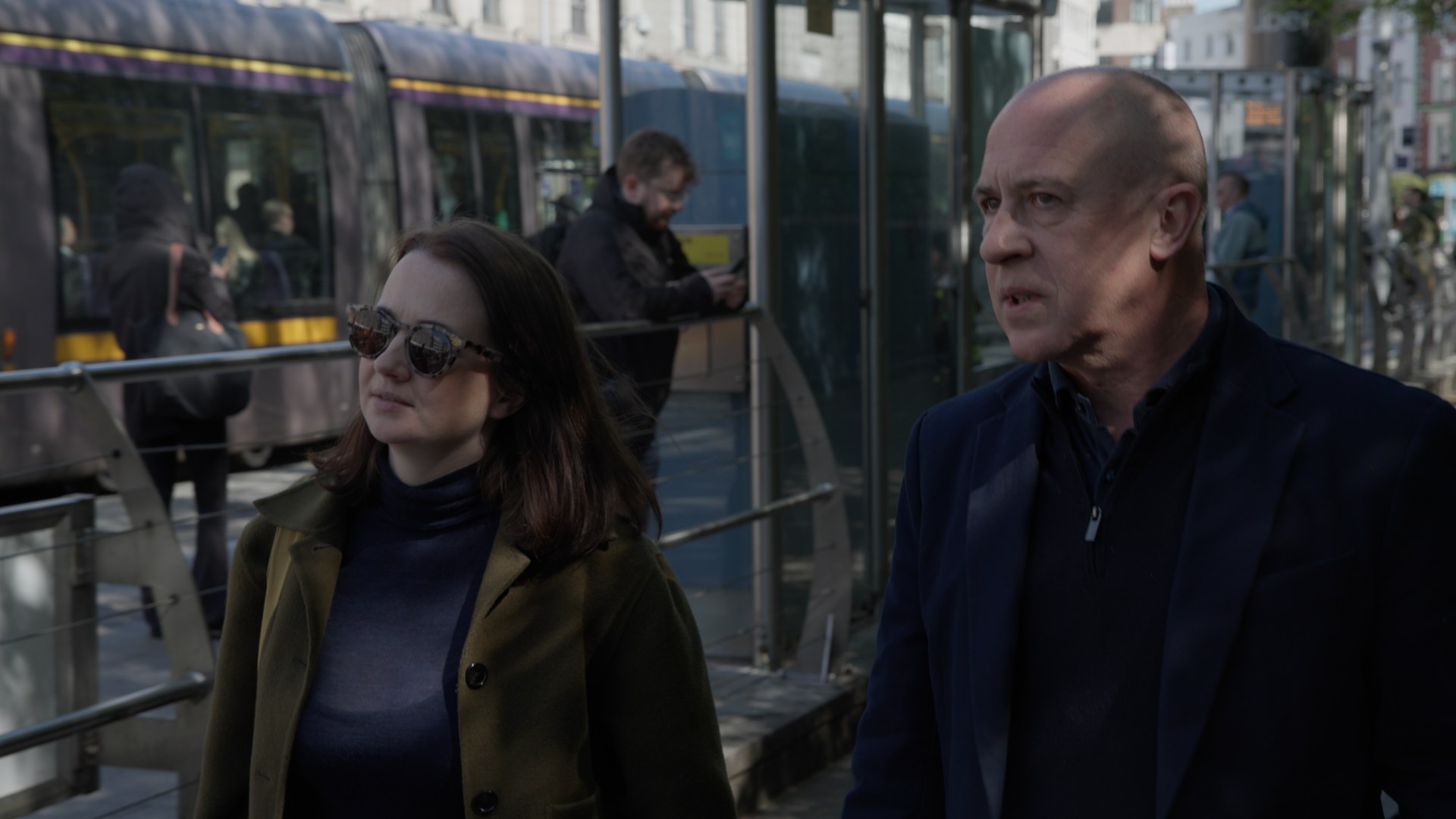 Two of the team talking on the street, a tram going past.