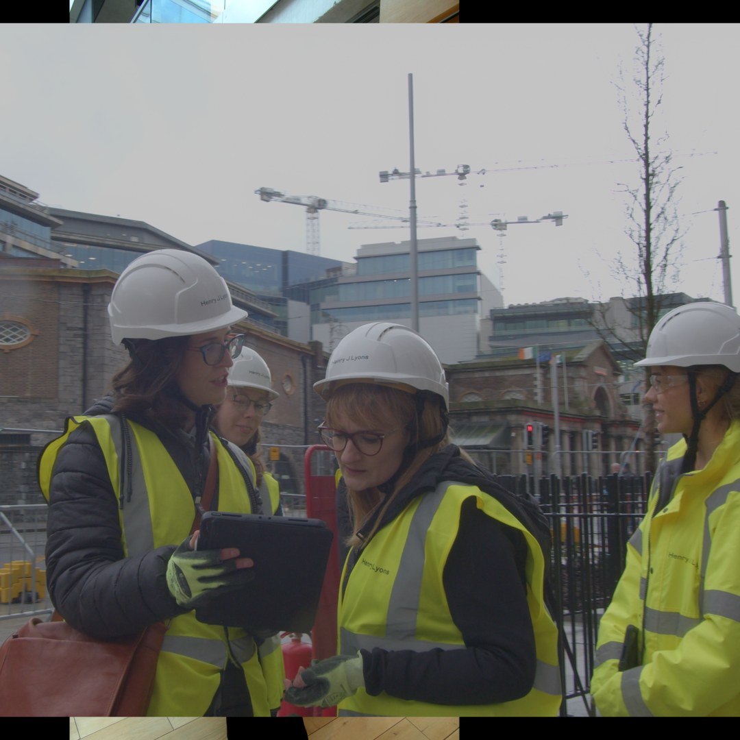 Three architects in hi-vis around a tablet, cranes behind them.