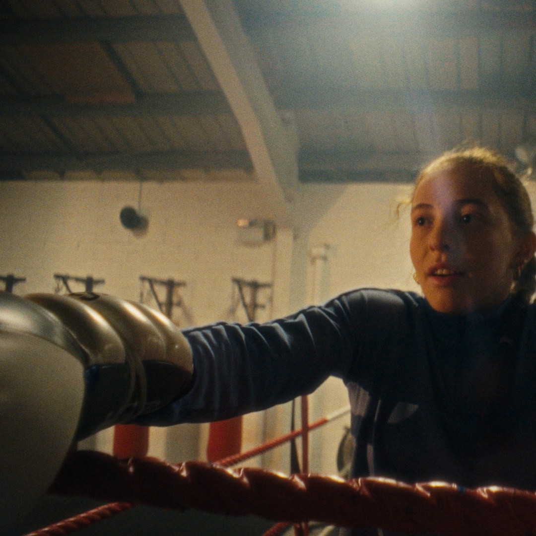 Leaning on the ropes, looking out of the ring.