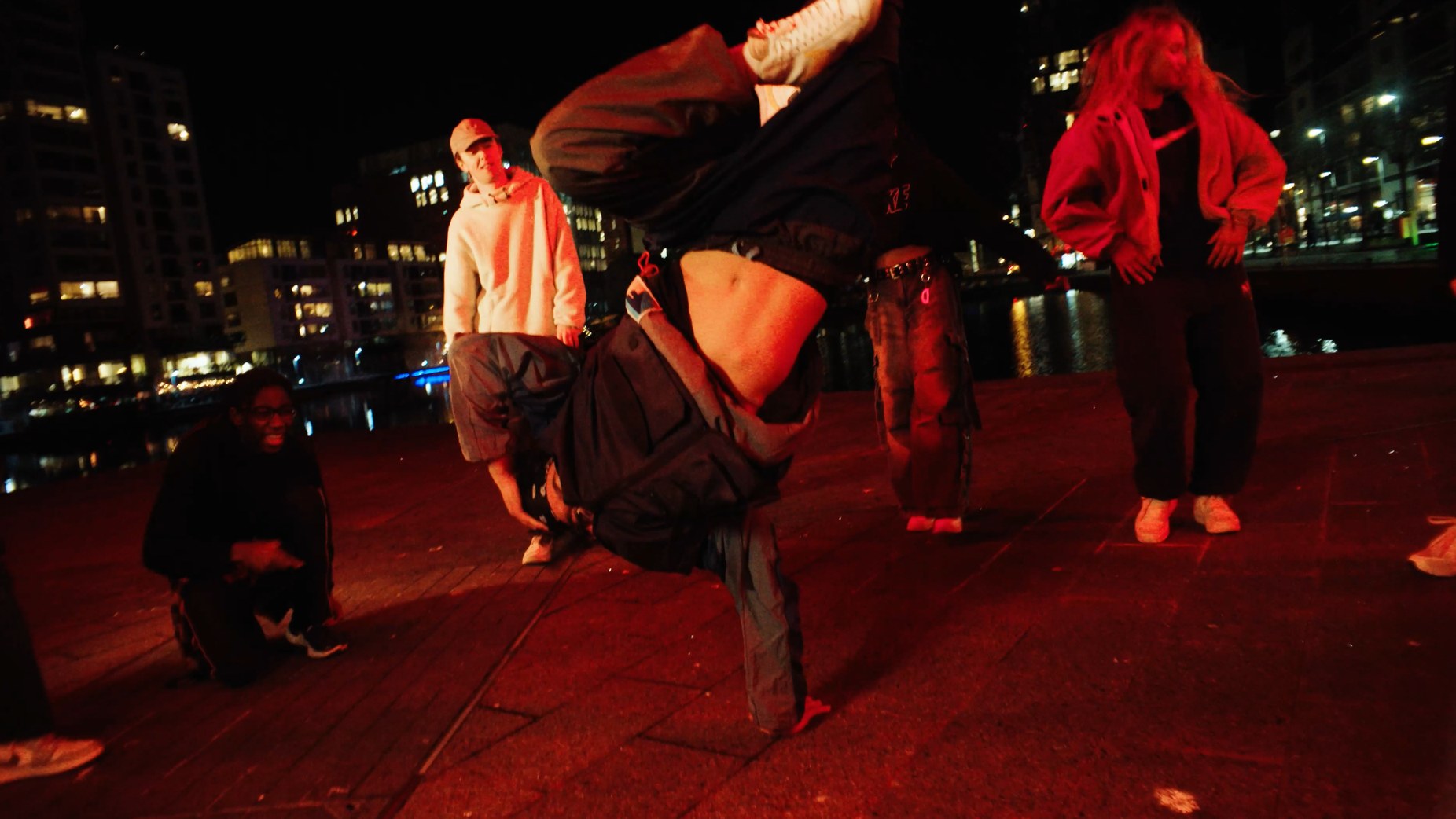 The dancer mid-freeze on the docks at night, the whole frame washed red.