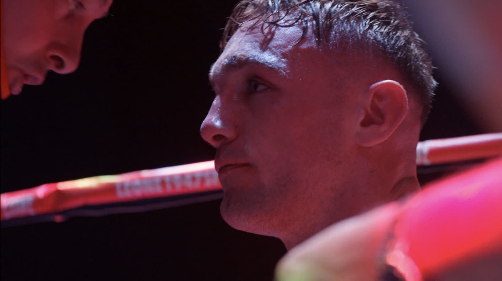 A boxer in the corner of the ring, lit red, listening to his corner between rounds.
