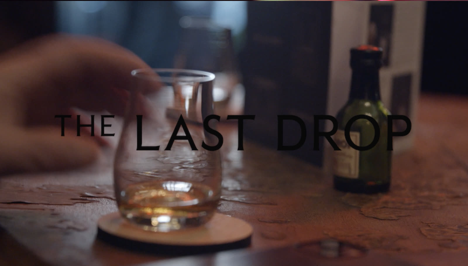 A bottle lit low against a dark ground, the last of the liquid caught in the light.