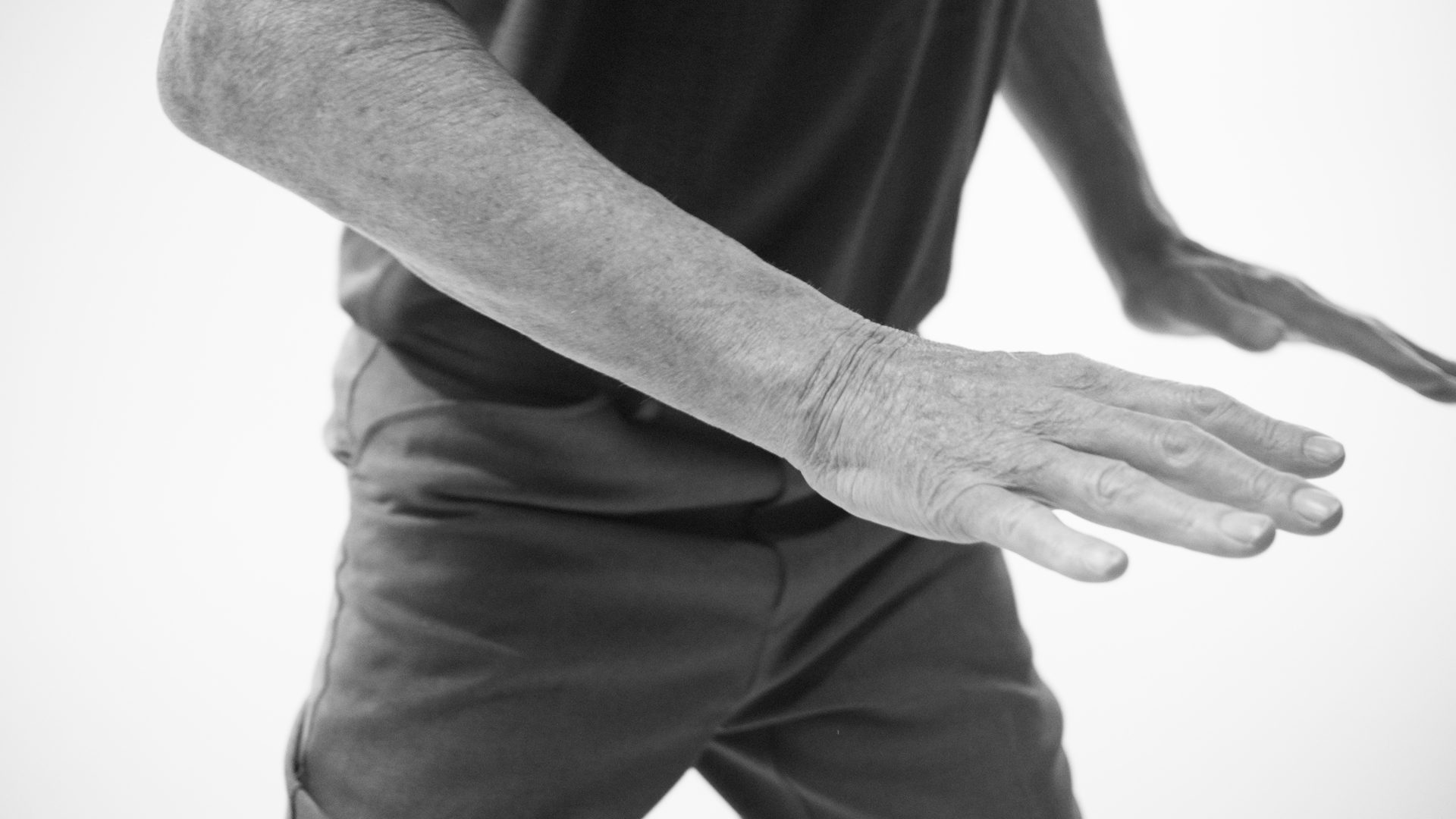 A dancer's hands and forearm in close-up, blurred mid-movement against white.